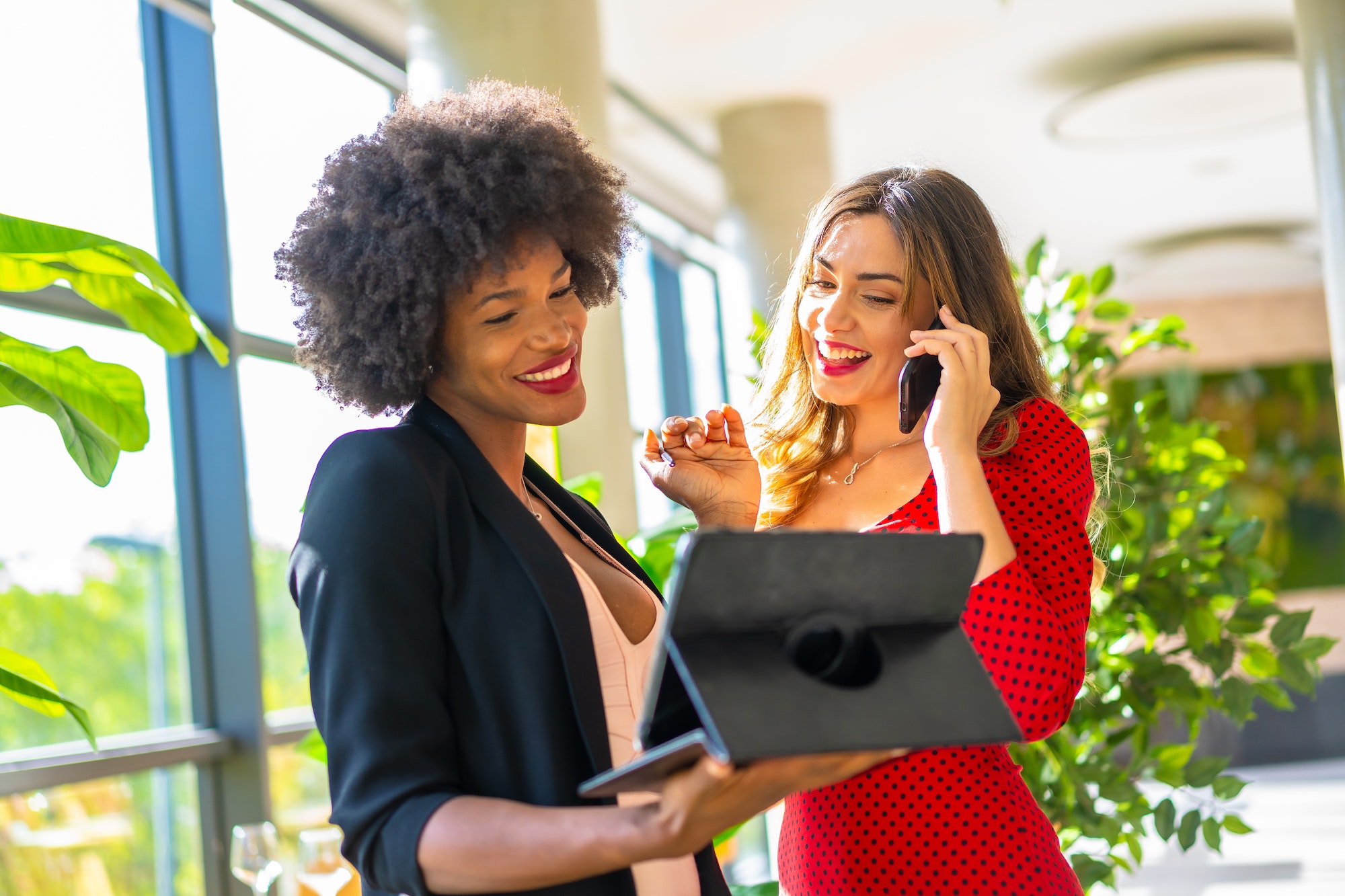 Caucasian blonde and black skinned girl with afro hair making a work video call with a tablet