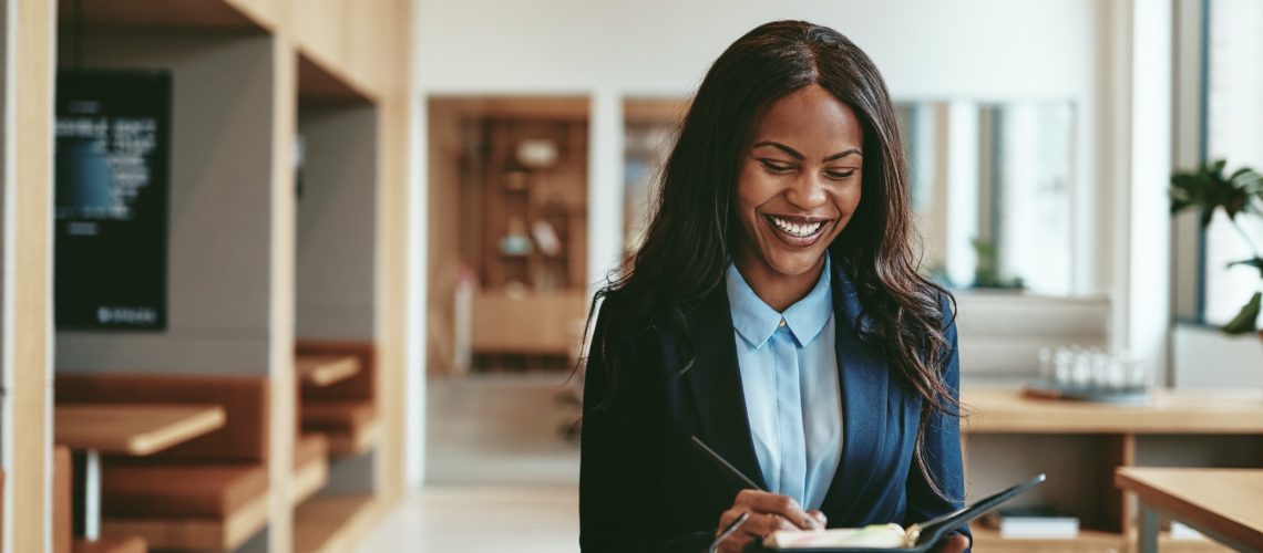 Laughing African American businesswoman walking in in office writing notes