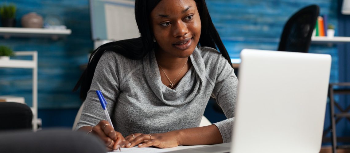 Woman taking notes at her laptop while planning business systems to overcome a growth plateau
